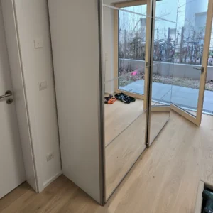 Vollständig montierter moderner weißer Kleiderschrank mit großen Schiebetüren aus Spiegelglas in einer hellen Berliner Wohnung.